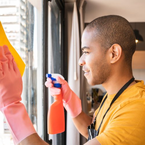 Male housekeeper cleaning glass window at home.